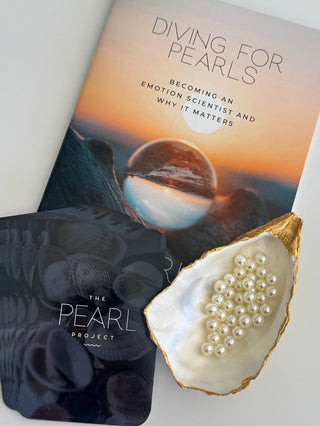 Flatlay of workbook titled 'Diving for Pearls' by The Pearl Project with the pearl project question cards and oyster shell with pearls inside