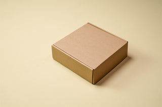 A plain closed kraft gift box on a soft beige background.