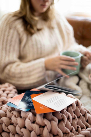 Woman holding coffee mug on couch with The Pearl Project mental health kit workbook and question cards