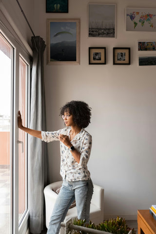 Woman holding cup of coffee looking hopefully out a window 